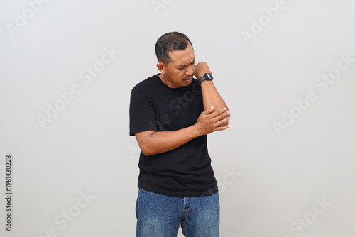 Fotografie A man stands isolated on a white background with pain in his elbow