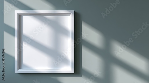 Blank white picture frame hangs on a solid colored wall illuminated by dramatic window shadows.