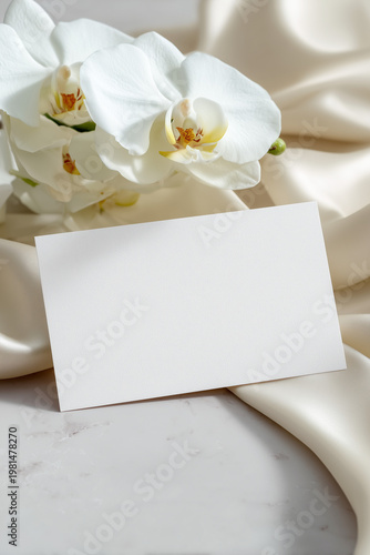 Wedding place card mockup with blank horizontal card and white orchid flowers on silk fabric background, elegant luxury stationery template