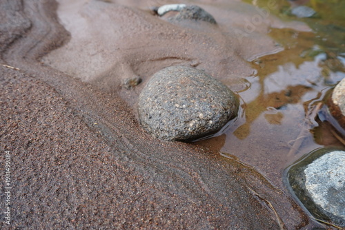 Close-up of smooth river stones on wet sand with rippling water