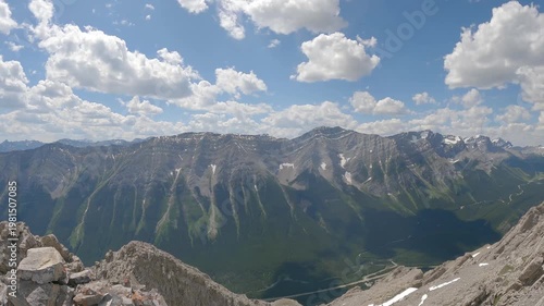 Scenic summer mountain landscape with dramatic rocky peaks, green forest valleys, and blue sky with clouds. View from a hiking trail overlooking the Canadian Rockies, capturing nature, adventure, and 