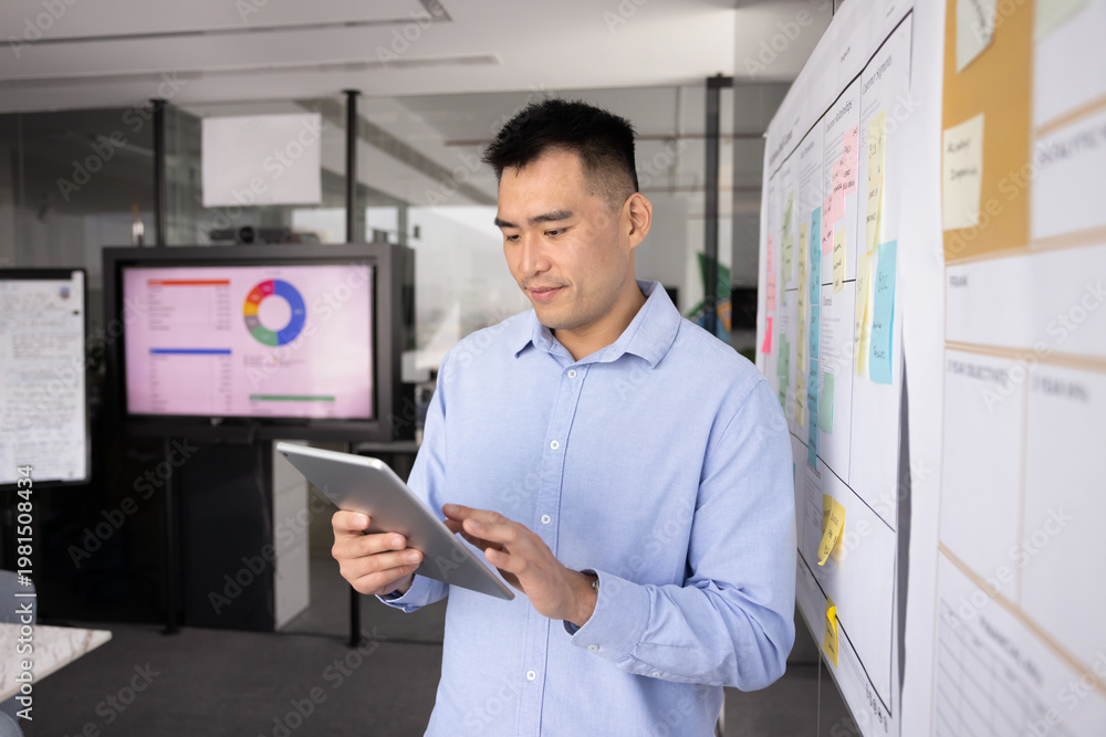 Fototapeta premium Project coordinator review. Confident young businessman stand near Kanban workflow model with tasks schedule on sticky notes check team work progress on digital tablet set deadlines priorities online