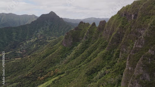 Aerial shot of typical Oahu's mountain peaks covered in lush tropical vegetation. Sharp ridgelines with view across the full mountain range