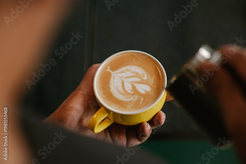 Barista holding a yellow cup of coffee latte with heart latte art