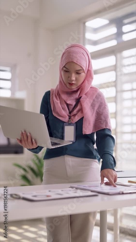 Asian adult woman professional analyzing business documents using laptop computer strategic planning modern office workspace productivity focus