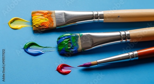 Close-up of three paintbrushes with colorful paint strokes against a blue backdrop