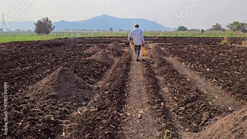A farmer walks through a plowed field, preparing the soil for planting. He passes piles of natural compost manure, which gets spread across the rows to enrich the earth & ensure a healthy, high yield.