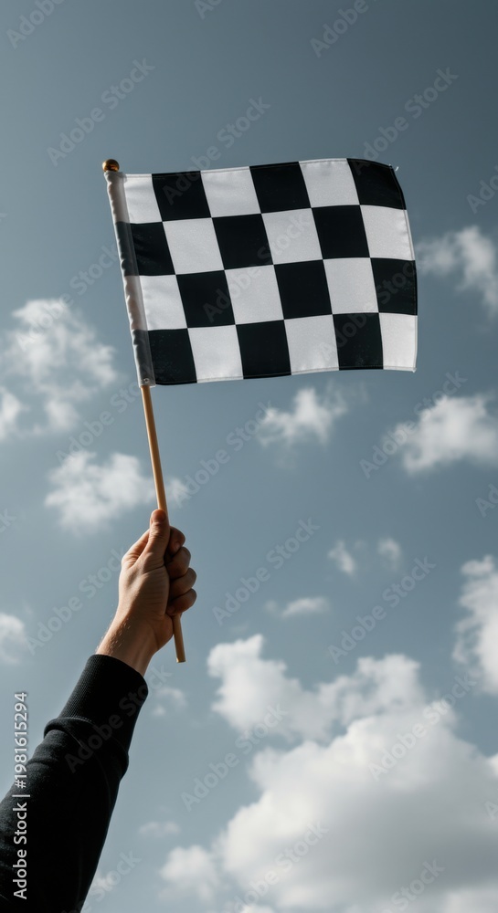 Fototapeta premium Person holding checkered race flag high against a blue sky for motorsport victory and achievement concept, low angle shot of hand with winning flag outdoors