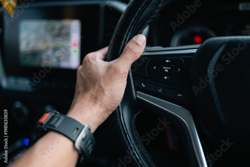 Close-up of Man’s Hand on Steering Wheel Driving a Modern Car with Navigation Map,A detailed close-up shot of a person's hand holding a leather steering wheel while driving. The background shows.