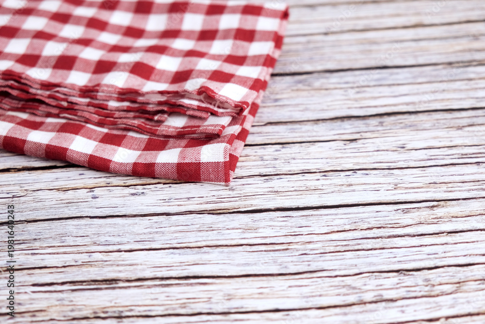 Obraz premium Red and white checkered cloth napkin rests on wood. Folds show soft texture and gentle creases. Rustic background adds charm and nostalgia. Ideal for kitchens, cafes, or picnic scenes