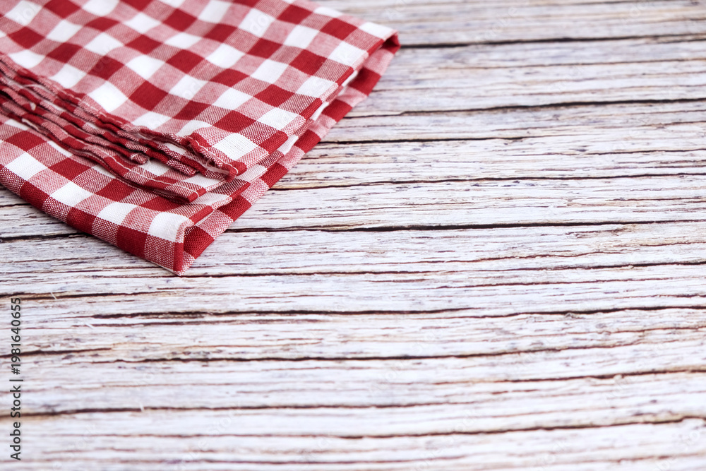 Obraz premium Red and white checkered cloth napkin rests on wood. Folds show soft texture and gentle creases. Rustic background adds charm and nostalgia. Ideal for kitchens, cafes, or picnic scenes