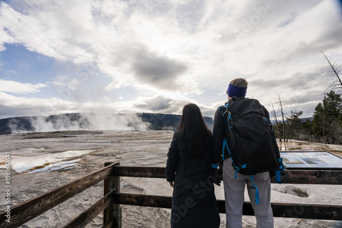 A scenic lifestyle shot of visitors exploring the unique geologic landscape and travertine terraces of Yellowstone under a dramatic, cloudy sky.