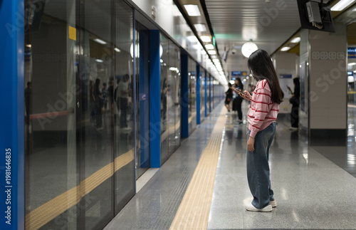 Asian child or kid girl waiting sky train or underground railways or people wearing face mask and earphones to playing smartphone in metro subway on railway station in street city for transport travel