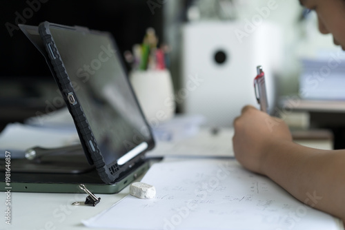 closeup computer tablet with hand child learn from home write on paper or young kid student doing homework to mathematics multiply calculate by study online class or people back to school learning