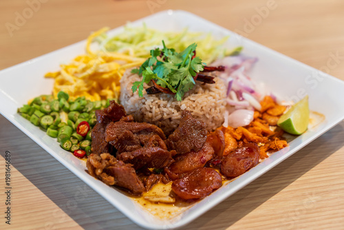 dried shrimp paste fried rice mixed with sausage egg or chopped omelet fresh and dried chili green long beans onion mango coriander lemon and sweet streaky pork for Thai street food on wooden table