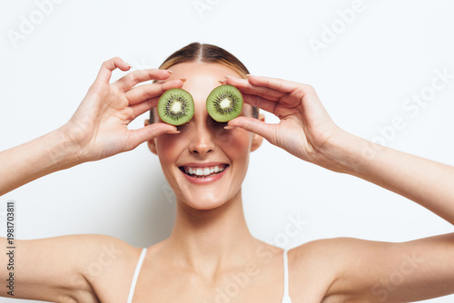 Woman kiwi fruit fresh healthy smiling eyes hands playful wellness concept, young woman holds kiwi halves over eyes on white studio background, showing healthy eating and joy