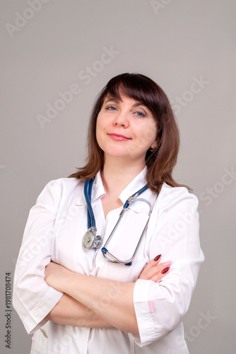 Smiling female doctor 40-50 years old in a white coat with a stethoscope on a gray background