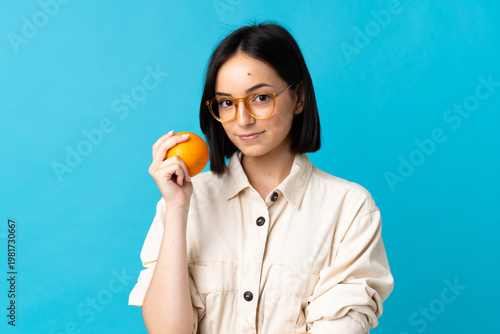 Young caucasian woman isolated on blue background holding an orange