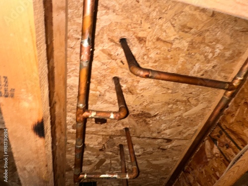 Copper plumbing lines routed through exposed wood framing in unfinished basement showing residential water supply system and construction detail