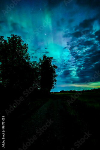 Northern öights dancing behinde the dark cloud over country landscape
