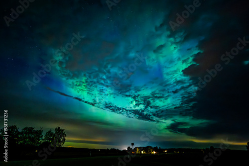 Northern öights dancing behinde the dark cloud over country landscape
