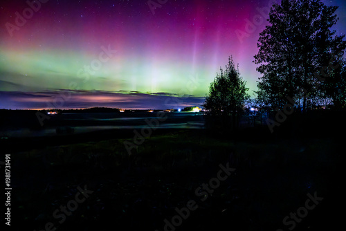 Northern öights dancing behinde the dark cloud over country landscape