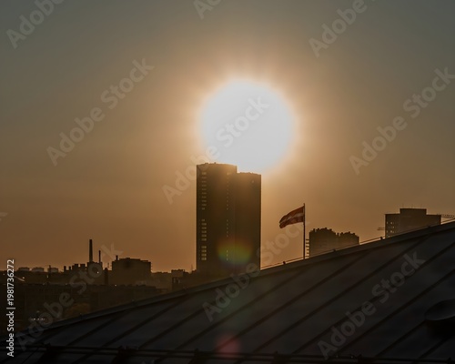 Foto Golden sunset over an urban skyline with silhouetted buildings and a Latvian flag