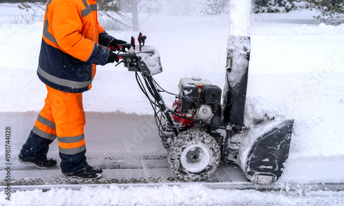 Worker in bright orange gear pushes snow blower