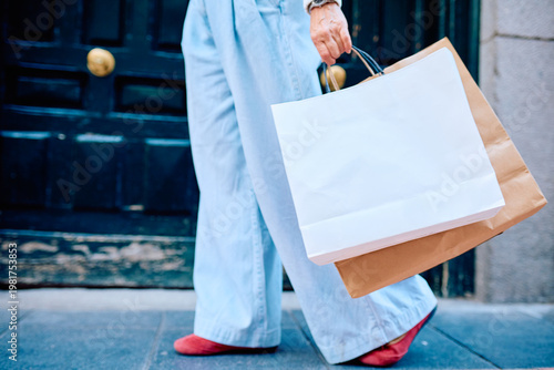 Tableau sur toile Woman's legs passing by a door, carrying unbranded paper shopping bags, demonstr