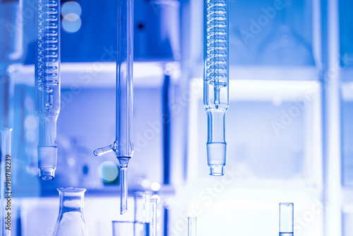 Close-up of laboratory glass condensers and distillation equipment under blue light, blurred background, concept of chemistry research and analytical setup.