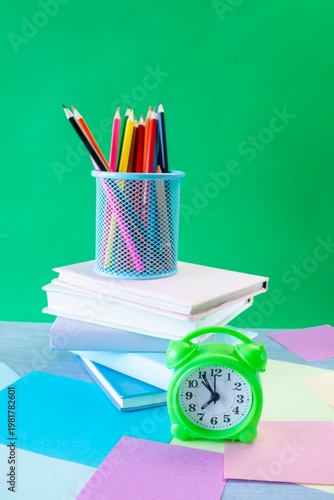 Study table with alarm clock, colorful pencils, colored paper and books. Learning concept, back to school