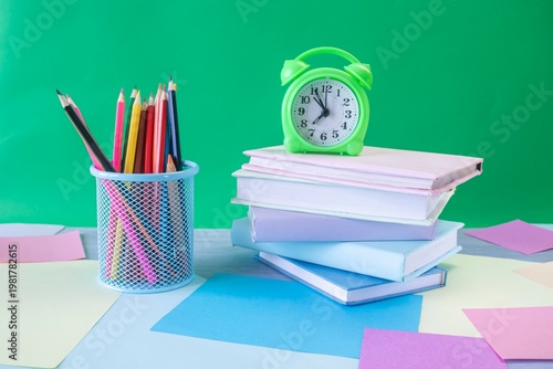 Study table with alarm clock, colorful pencils, colored paper and books. Learning concept, back to school