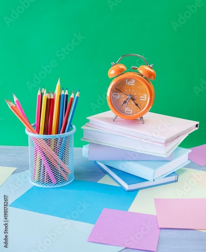 Study table with alarm clock, colorful pencils, colored paper and books. Learning concept, back to school