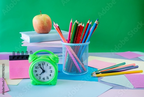 Study table with alarm clock, colorful pencils, colored paper and books. Learning concept, back to school