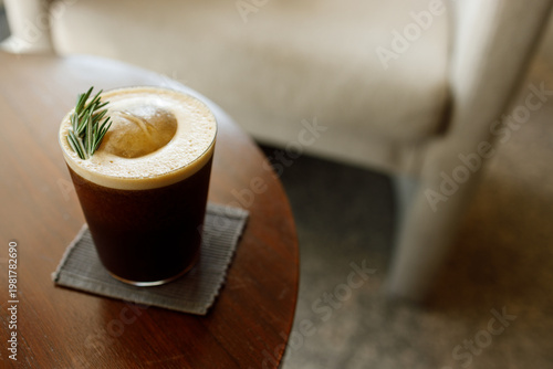 Cup of creation coffee Mocktail drink decorated with rosemary and foam on wooden table.