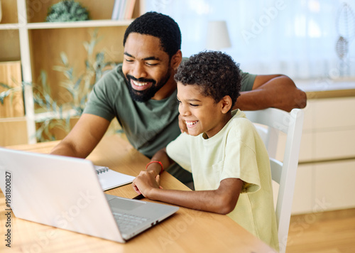 Father and son doing homework with laptop at home. Father and teenage son using laptop. Boy and dad sitting at home working with notebook