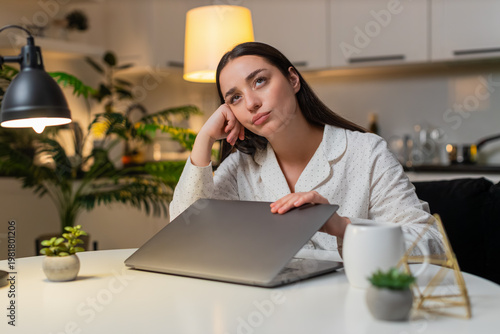 Young woman at night home shuts laptop after work feels burnout wants pause takes breath. Caucasian girl on sofa at table at evening looks tired says enough rubs temples needs break rests eyes closed.