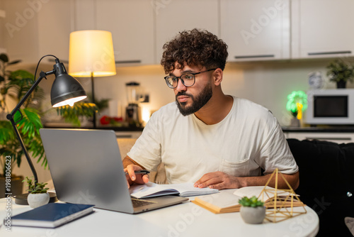Canvas Print Arabian man at home studies online on laptop watches lesson writes notes smiles learns for exam