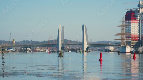 Modern bascule bridge over calm harbor water with ships and city skyline in daylight
