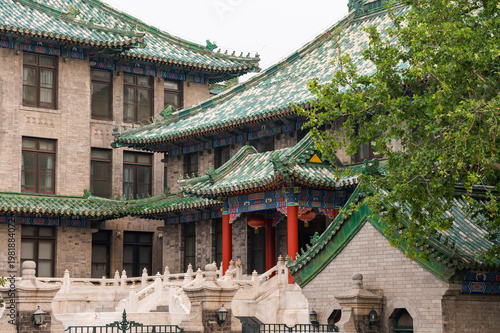 A historic building with distinctive green-tiled roofs stands at a city intersection in Beijing, traditional Chinese architectural elements and a pedestrian crosswalk. Beijing, China 29 May 2025