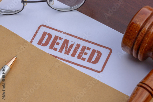 Close up of a document stamped with red DENIED word near a judge gavel and eyeglasses