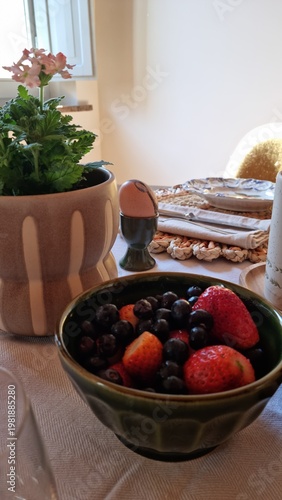 Bowl of fresh berries with soft-boiled egg and crispbread near window with houseplant