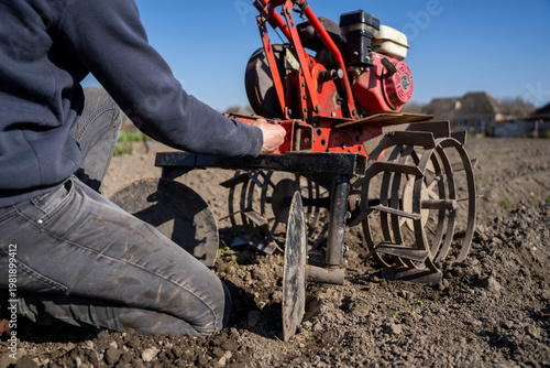 Tableau sur toile Person installing hiller attachment on walk behind tractor, agricultural implement used for forming soil ridges during field cultivation