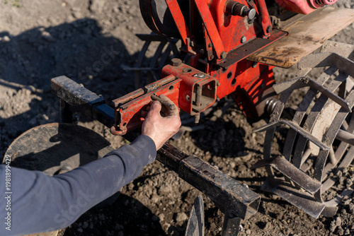 Bild auf Leinwand Person installing hiller attachment on walk behind tractor, agricultural implement used for forming soil ridges during field cultivation