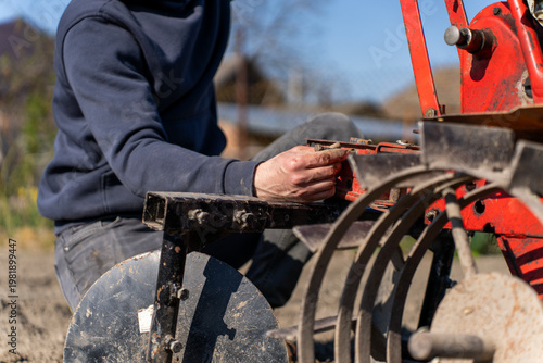 Tableau sur toile Person installing hiller attachment on walk behind tractor, agricultural implement used for forming soil ridges during field cultivation
