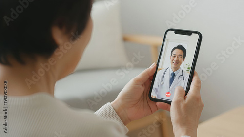 スマホでビデオ通話をしながら医師の診察を受ける高齢女性　自宅でオンライン診療・遠隔医療イメージ