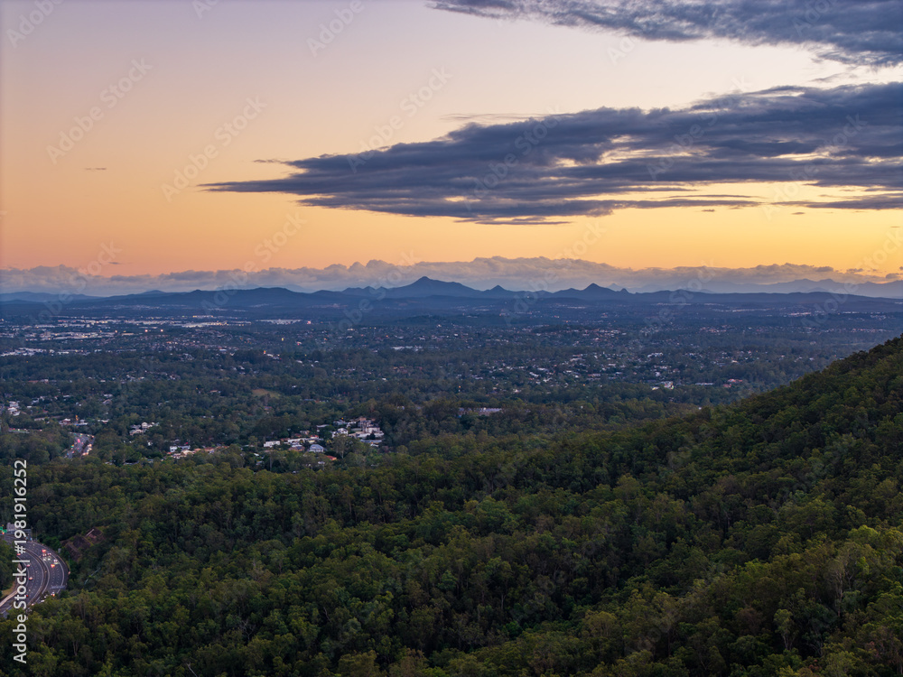 Fototapeta premium Breathtaking twilight panorama of Brisbane city, its sprawling suburbs, and distant mountains under a radiant sunset sky.