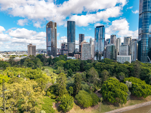 Fotografia An aerial perspective of the lush Brisbane City Botanic Gardens contrasting with the modern central business district skyline under a bright, cloud-dotted sky