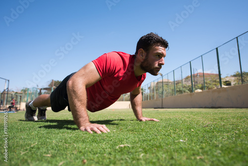 Schilderij op canvas Man doing push-ups outdoors at a CrossFit style open-air fitness gym with focuse