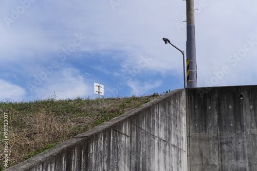 Urban Concrete Wall Next to a Green Grassy Hill with a Street Light and Blue Sky